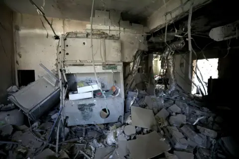 Andalou via Getty Images There is rubble on the floor, the walls are damaged, a large piece of equipment has been destroyed and cables hang from the ceiling.
