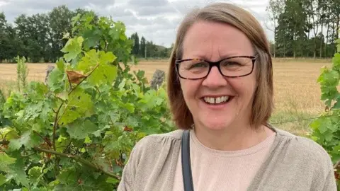 NHS Sussex Woman smiles at the camera,  wearing glasses with green fields in the background