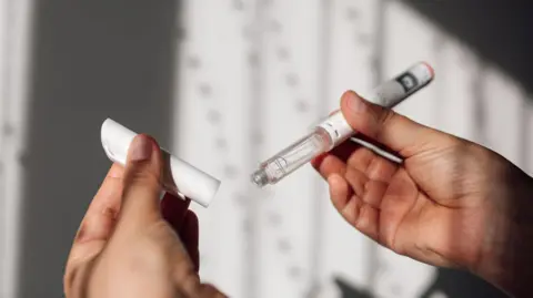 Getty Images Close up of hands holding a vial containing clear liquid with its cap off.