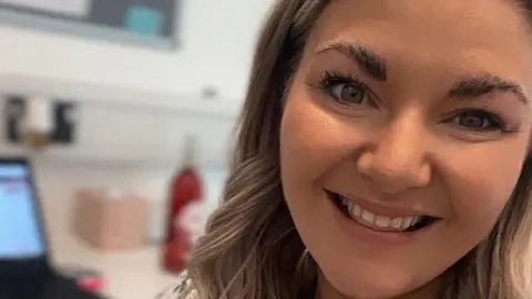 Siobhan Gorman A selfie of Siobhan Gorman who has long wavy blonde hair and  is smiling. She is in an office. 