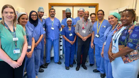 UHNM A group of medical staff are gathered together in hospital scrubs and are smiling at the camera.