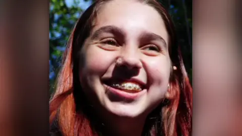 Family handout A girl with dyed red hair is smiling. She is wearing braces on her teeth. 
