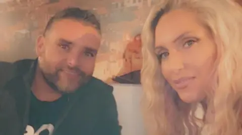 Jessica Mason Jessica, who has long blonde hair, smiles in a selfie with her husband Dan, who is wearing a black jumper and has short silvery hair and stubble. 