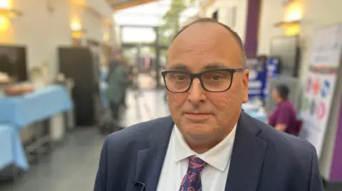 BBC A man in a suit, paisley tie and black-rimmed glasses