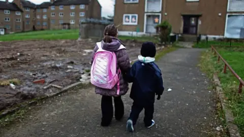 Getty Images Two children walk hand in hand in a run-down housing estate 