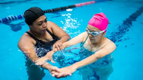 Getty Images A woman is being given swimming lessons in a pool.