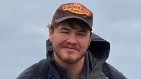 Family Handout William is wearing a brown DSquared cap and navy blue Berghaus anorak. He is smiling at the camera.